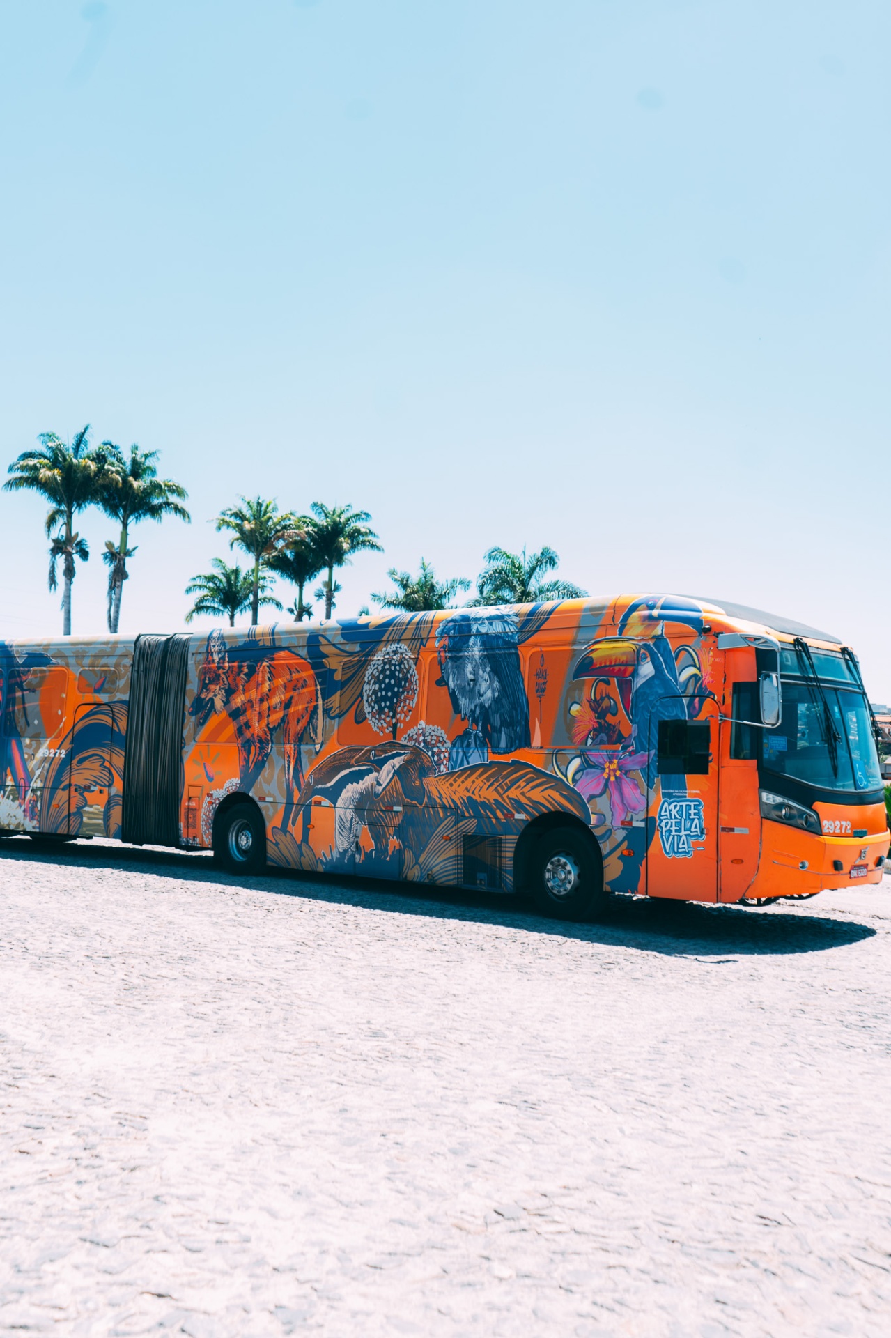 Ônibus Arte Pela Via envelopado pelo artista Kaká estacionado entre palmeiras
